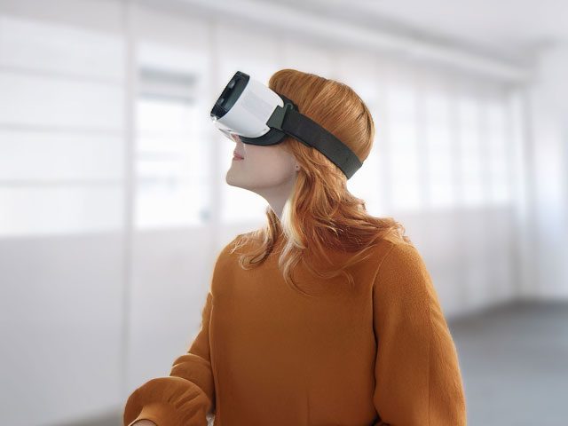 Eine Frau steht in einem weißen, leeren Raum und schaut mit einer VR Brille nach rechts oben