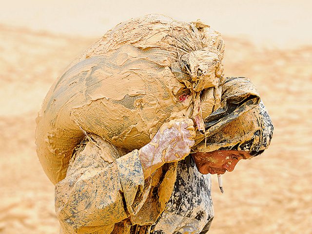 Ein Arbeiter trägt einen verschlammten Sack auf dem Rücken