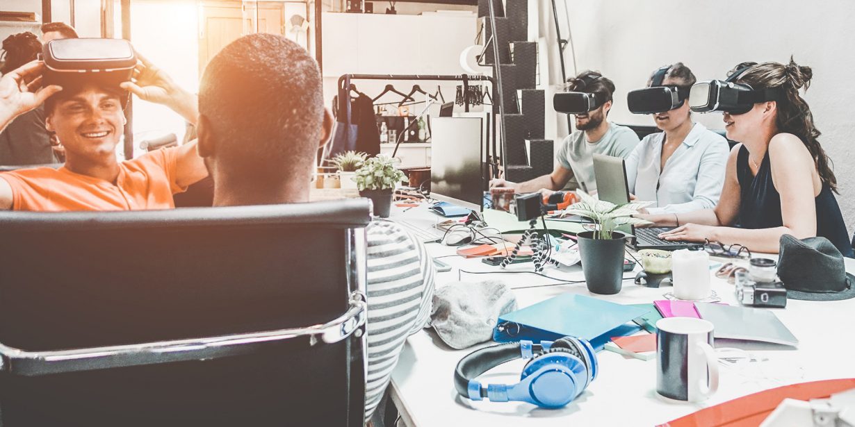 Eine Gruppe junger Menschen sitzt um einen Tisch und trägt teilweise VR-Brillen