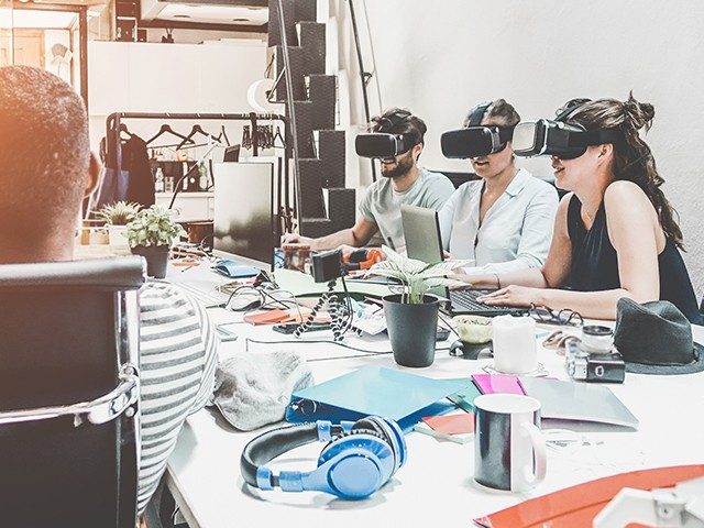 Eine Gruppe junger Menschen sitzt um einen Tisch und trägt teilweise VR-Brillen