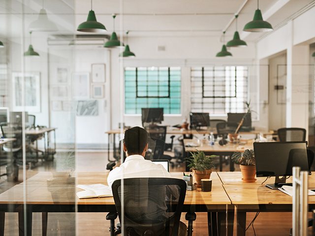 Ein großes Büro in dem nur ein Mitarbeiter sitzt und arbeitet.