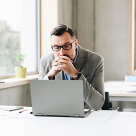 Getty Images/djedzura Ein Mann blickt nachdenklich auf ein Laptop