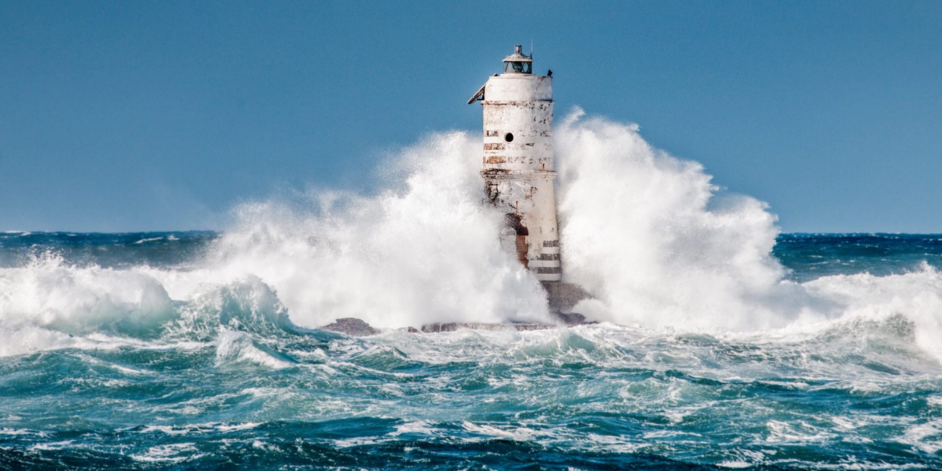 Weißer Leuchtturm in schwerer See bei sonnigem Wetter.