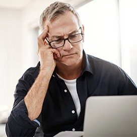 Mann in blauem Hemd schaut grübelnd auf seinen Laptop