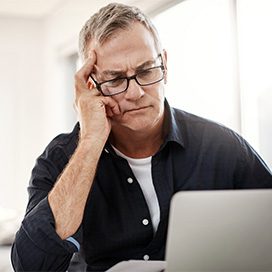 Mann in blauem Hemd schaut grübelnd auf seinen Laptop